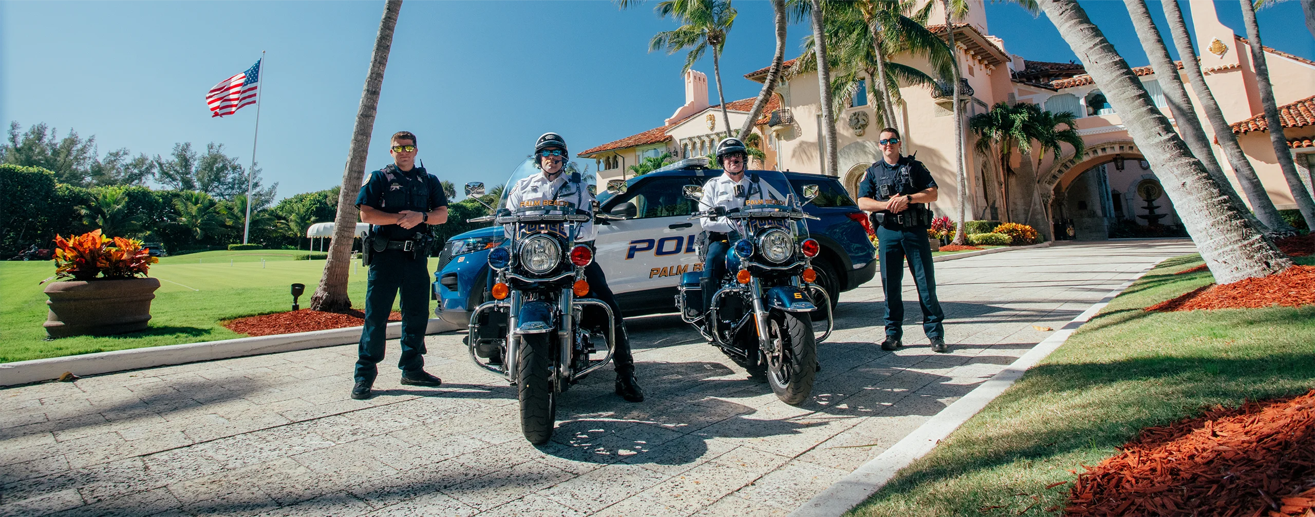 Police officers on motorcycles stand in front of a Palm Beach mansion.