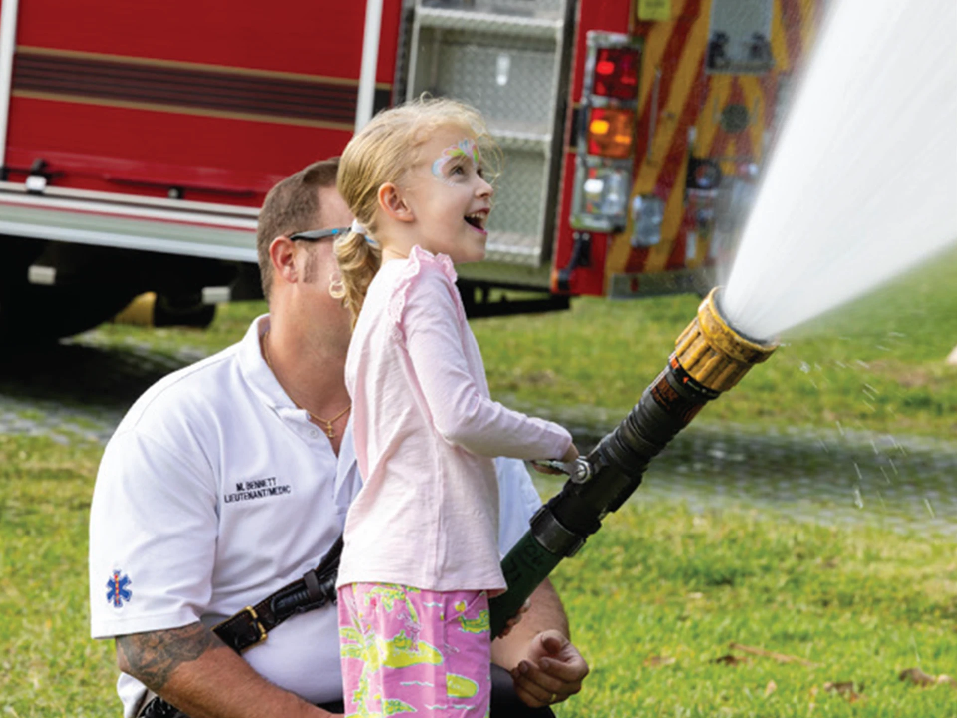 Man and a little girl enthusiastically spraying water from a fire hose.
